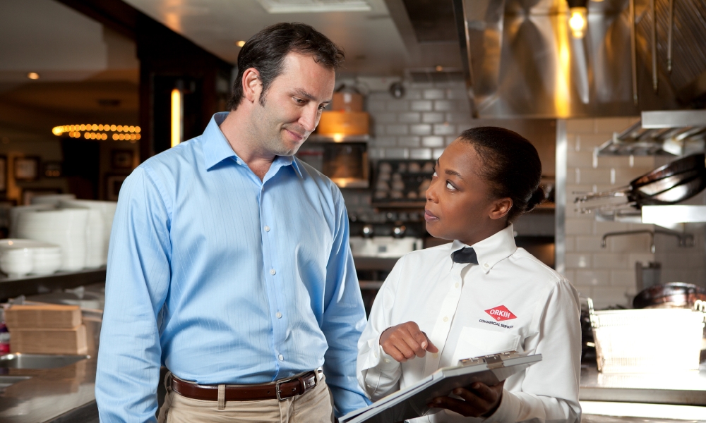 Commercial Orkin Pro talking to a foodservice customer in a restaurant kitchen about drain care