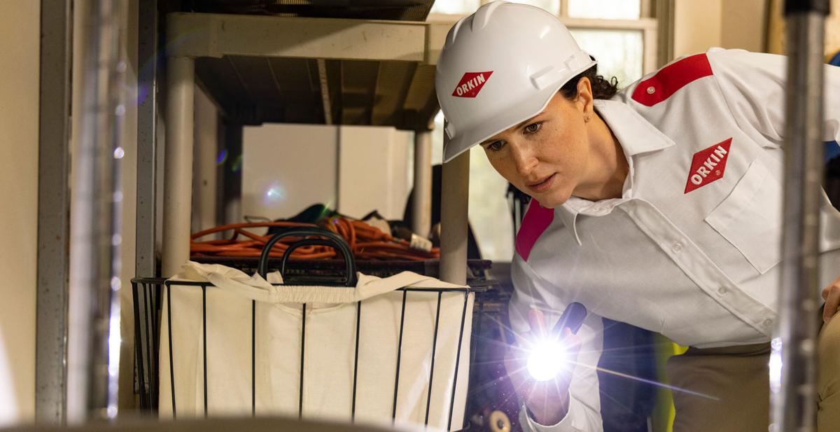 An Orkin Pro inspecting for rodents with a flashlight in the garage of a customer's home